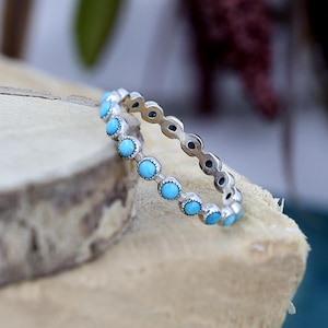 Op de afbeelding: Een zilveren ring met een rij turquoise stenen in een bezel setting.