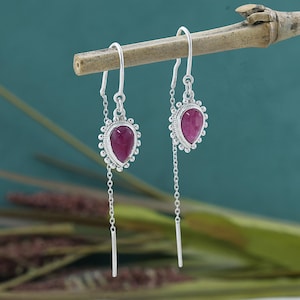 Könnte beinhalten: Ein Paar silberne Ohrringe mit rosa tropfenförmigen Steinen. Die Ohrringe haben eine zarte Kette, die von dem Stein herabhängt.