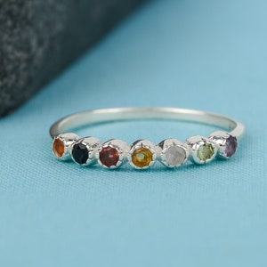 Può includere: Un anello d'argento con sette pietre preziose colorate disposte in fila. Le pietre preziose sono rossa, nera, arancione, gialla, bianca, verde e viola.