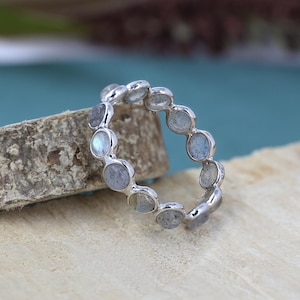 May include: A silver ring with a band of round, iridescent labradorite stones.