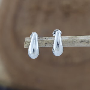 May include: A pair of polished silver stud earrings shaped like smooth, elongated teardrops. Each earring features a reflective, metallic surface and a secure post backing, presenting a clean, minimalist design with a rounded base and tapered top.