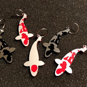 Könnte beinhalten: Fünf verschiedene Koi-Fisch-Schlüsselanhänger. Jeder Schlüsselanhänger ist aus Metall und hat ein anderes Farbmuster. Die Schlüsselanhänger haben alle die Form eines Koi-Fisches mit einem Ring, der oben befestigt ist.
