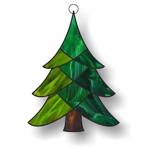 Puede incluir: Adorno de árbol de Navidad de vidrieras. El árbol está compuesto por varios tonos de vidrio verde, con un tronco marrón y un lazo de metal negro para colgar. El vidrio tiene un aspecto texturizado y veteado.