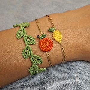 May include: Three macrame bracelets featuring a green vine design, a round orange fruit motif, and a yellow lemon shape. The bracelets are constructed from thin, knotted cord in vibrant shades of green, orange, and yellow, creating a detailed botanical and fruit-themed set of wrist accessories.
