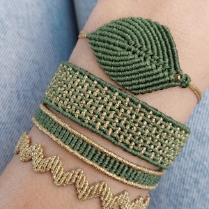 Könnte beinhalten: Vier grüne und goldene Freundschaftsarmbänder. Ein Armband ist in Form eines Blattes, eines ist mit einem gewebten Muster, eines ist ein durchgehendes Band mit goldener Einfassung und eines ist mit einem Wellenmuster.
