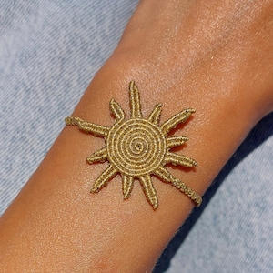 Può includere: Un braccialetto dorato a forma di sole realizzato con cordoncino intrecciato.