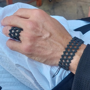 Pode incluir: Um bracelete e um anel pretos tecidos com um padrão geométrico. O bracelete tem um fecho de nó.