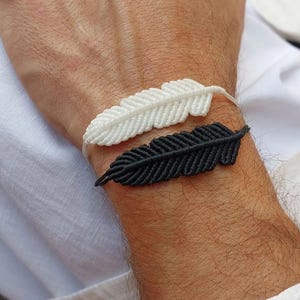 Può includere: Due braccialetti a forma di piuma sul polso di una persona. Un braccialetto è bianco e l'altro è nero.