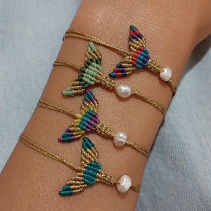Può includere: Quattro braccialetti in cordoncino dorato con ciondoli a forma di coda di sirena colorati e dettagli in perle bianche.