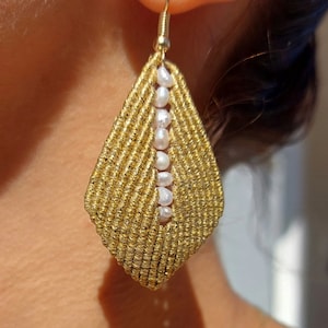 May include: Gold and white pearl earrings with a teardrop shape. The earrings are made with a woven cord and feature a row of pearls down the center.