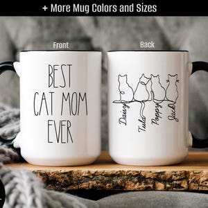 May include: A white ceramic mug with a black handle and rim. The front features the black text 'BEST CAT MOM EVER'. The back displays a continuous line drawing of four cats with the names 'Daisy', 'Tula', 'Poppy', and 'Jack' written below them.