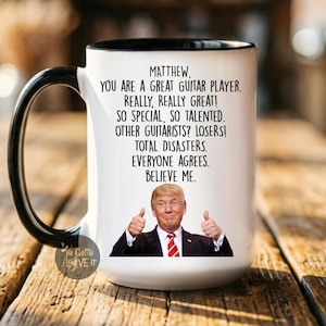 Puede incluir: Taza de cer&aacute;mica blanca con asa y borde negros. La taza presenta el texto "MATTHEW, YOU ARE A GREAT GUITAR PLAYER. REALLY, REALLY GREAT!" y una imagen de un hombre levantando el pulgar.