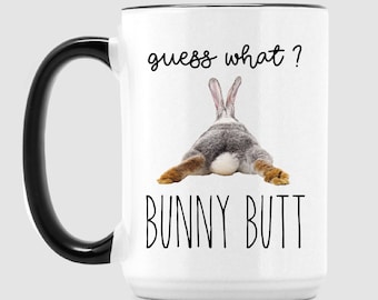 Può includere: Tazza in ceramica bianca con manico e bordo neri. La tazza presenta il testo "guess what?" sopra un'immagine del posteriore di un coniglio, con le parole "BUNNY BUTT" sotto. La tazza è etichettata "15OZ MUG".