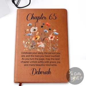 May include: A brown leather journal with the text "Chapter 65" and the name "Deborah". The journal features a floral design and inspirational text. Black glasses and a succulent plant are also visible.