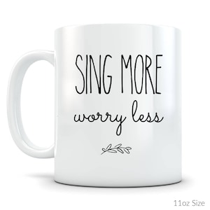 May include: White ceramic coffee mug with black text that reads "Sing More Worry Less" and a small twig design.