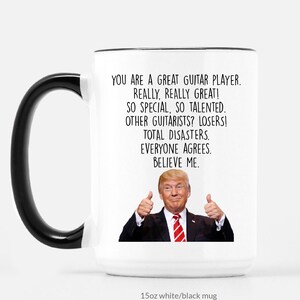 Puede incluir: Taza de cer&aacute;mica blanca con asa y borde negros. La taza presenta el texto "YOU ARE A GREAT GUITAR PLAYER. REALLY, REALLY GREAT!" y una imagen de un hombre haciendo una se&ntilde;al de pulgar hacia arriba.