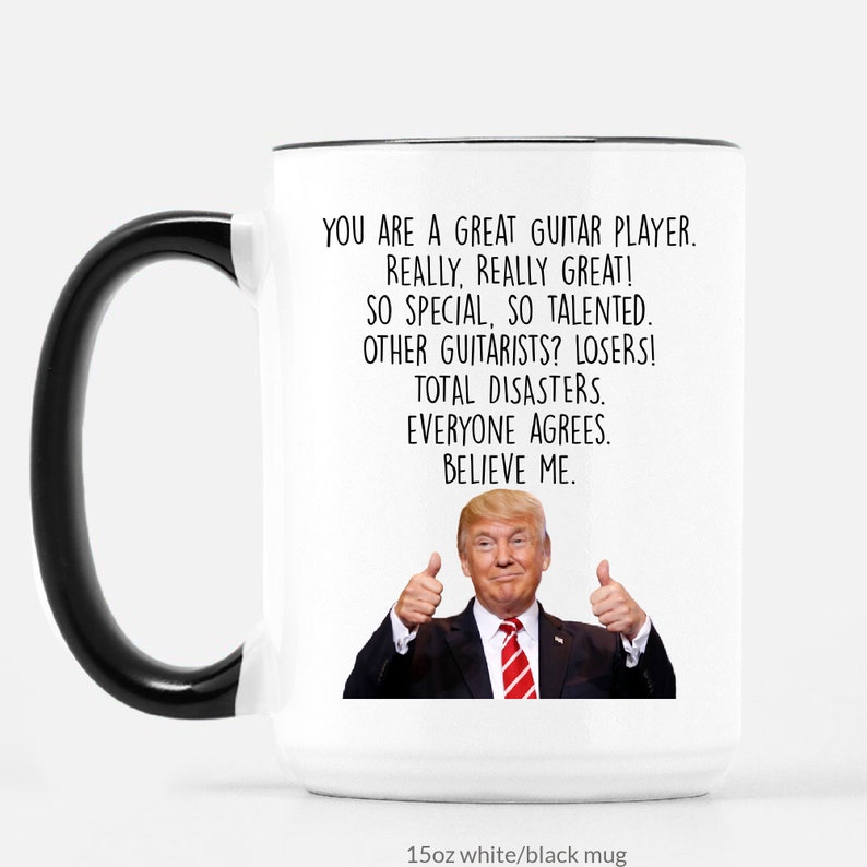 Puede incluir: Taza de cer&aacute;mica blanca con asa y borde negros. La taza presenta el texto "YOU ARE A GREAT GUITAR PLAYER. REALLY, REALLY GREAT!" y una imagen de un hombre haciendo una se&ntilde;al de pulgar hacia arriba.