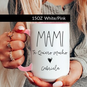 May include: White ceramic mug with a pink rim and handle. The mug has black text that reads "MAMI Te Quiero Mucho" with a heart symbol and the name "Gabriela".