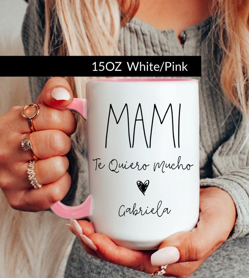 May include: White ceramic mug with a pink rim and handle. The mug has black text that reads "MAMI Te Quiero Mucho" with a heart symbol and the name "Gabriela".