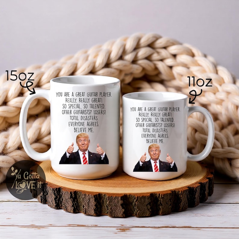 Puede incluir: Dos tazas de cer&aacute;mica blanca con texto negro y la imagen de un hombre haciendo una se&ntilde;al de pulgar hacia arriba. El texto dice: "ERES UN GRAN GUITARRISTA. &iexcl;REALMENTE, REALMENTE GENIAL!" Una taza es de 425 ml, la otra de 312 ml. Las tazas est&aacute;n sobre una superficie de madera.