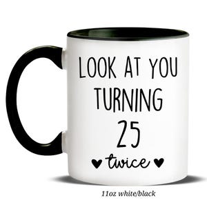 May include: White ceramic mug with a black handle and rim. The mug features the text "LOOK AT YOU TURNING 25 twice" in black, with two heart symbols. The bottom of the mug reads "11oz white/black".