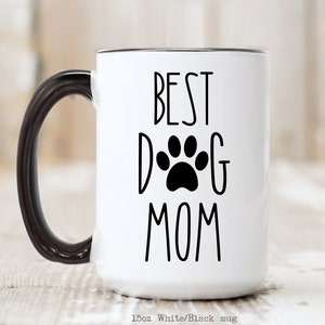 May include: White ceramic mug with a black handle and black rim. The mug has the text "BEST DOG MOM" in black lettering with a black paw print in the center of the "D" and "G".
