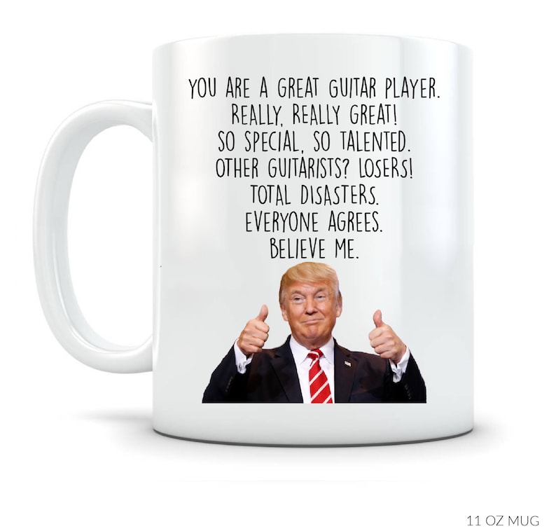 May include: White 11 oz mug featuring a humorous design. The mug displays a photo of Donald Trump giving a thumbs-up, along with text that reads: 'You are a great guitar player. Really, really great! So special, so talented. Other guitarists? Losers! Total disasters. Everyone agrees. Believe me.' The design is suitable for guitar players and features a playful, sarcastic tone.