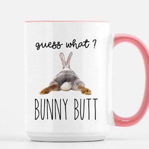 Puede incluir: Taza de cer&aacute;mica blanca con interior y asa rosa. La taza presenta el texto "guess what?" encima de una imagen del trasero de un conejo, con las palabras "BUNNY BUTT" debajo.