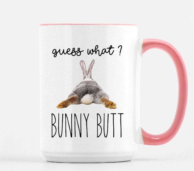 Puede incluir: Taza de cer&aacute;mica blanca con interior y asa rosa. La taza presenta el texto "guess what?" encima de una imagen del trasero de un conejo, con las palabras "BUNNY BUTT" debajo.