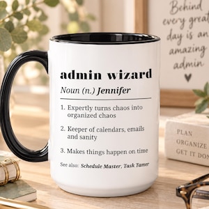 May include: A white ceramic mug with a black handle and interior, featuring the black printed text: admin wizard, Noun (n.) Jennifer, 1. Expertly turns chaos into organized chaos, 2. Keeper of calendars, emails and sanity, 3. Makes things happen on time, See also: Schedule Master, Task Tamer.