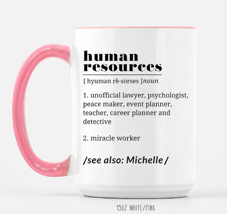 May include: White ceramic mug with a pink handle. The mug features a black graphic that reads "human resources" with a definition and the text "see also: Michelle". The mug is 15 oz and is white with a pink rim.