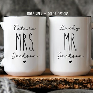 Puede incluir: Dos tazas de cer&aacute;mica blanca con asas y bordes negros. La taza izquierda presenta el texto negro Future MRS. Jackson con un peque&ntilde;o coraz&oacute;n. La taza derecha presenta el texto negro Lucky MR. Jackson con un peque&ntilde;o coraz&oacute;n. Texto arriba: MORE SIZES + COLOR OPTIONS.