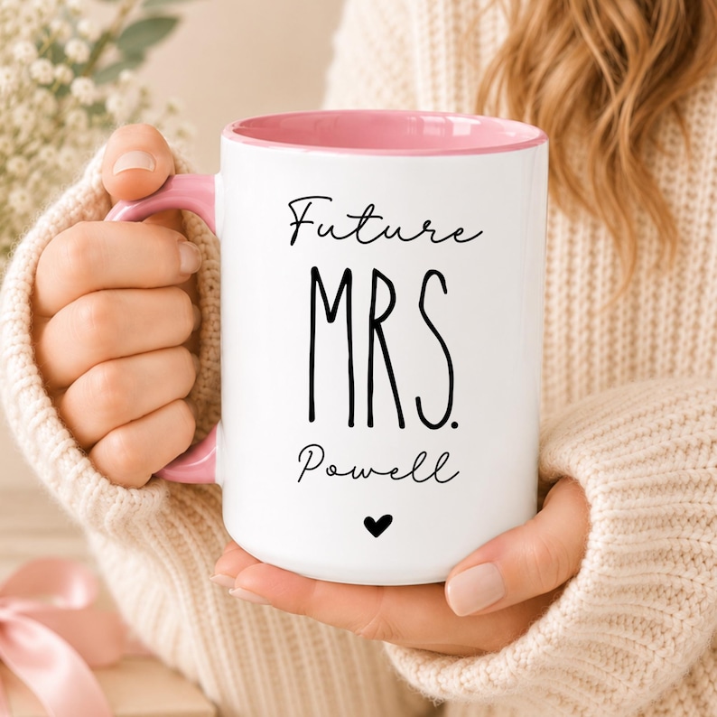 Puede incluir: Una taza de cer&aacute;mica blanca con interior y asa de color rosa suave. El frente presenta el texto negro Future MRS. Powell con un peque&ntilde;o icono de coraz&oacute;n negro centrado debajo del nombre. El dise&ntilde;o est&aacute; impreso en una fuente simple y limpia.