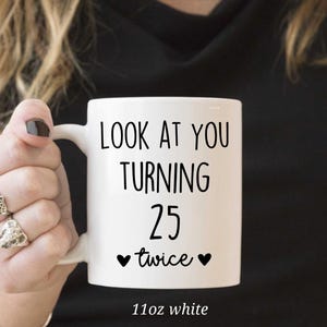 May include: White ceramic mug with the text "LOOK AT YOU TURNING 25 twice" in black. The mug has a black heart on each side of the word "twice". The mug is 11oz.