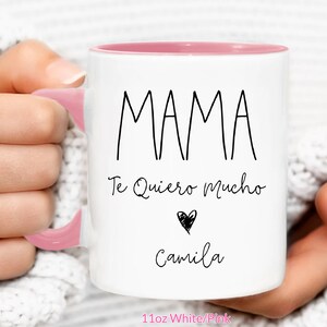 May include: White ceramic mug with a pink rim and handle. The mug has black text that reads "MAMA Te Quiero Mucho" with a black heart and the name "Camila" underneath. The mug is 11oz and is white with a pink rim.