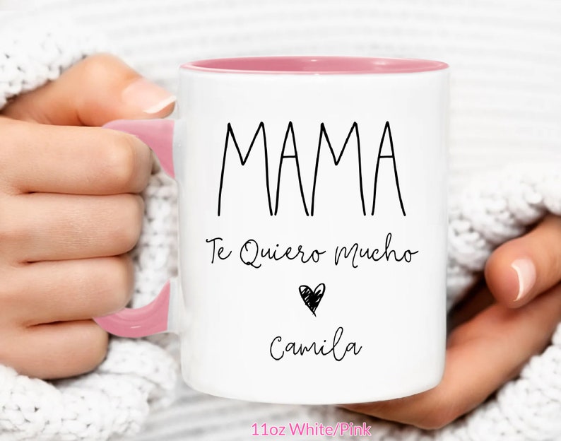 May include: White ceramic mug with a pink rim and handle. The mug has black text that reads "MAMA Te Quiero Mucho" with a black heart and the name "Camila" underneath. The mug is 11oz and is white with a pink rim.