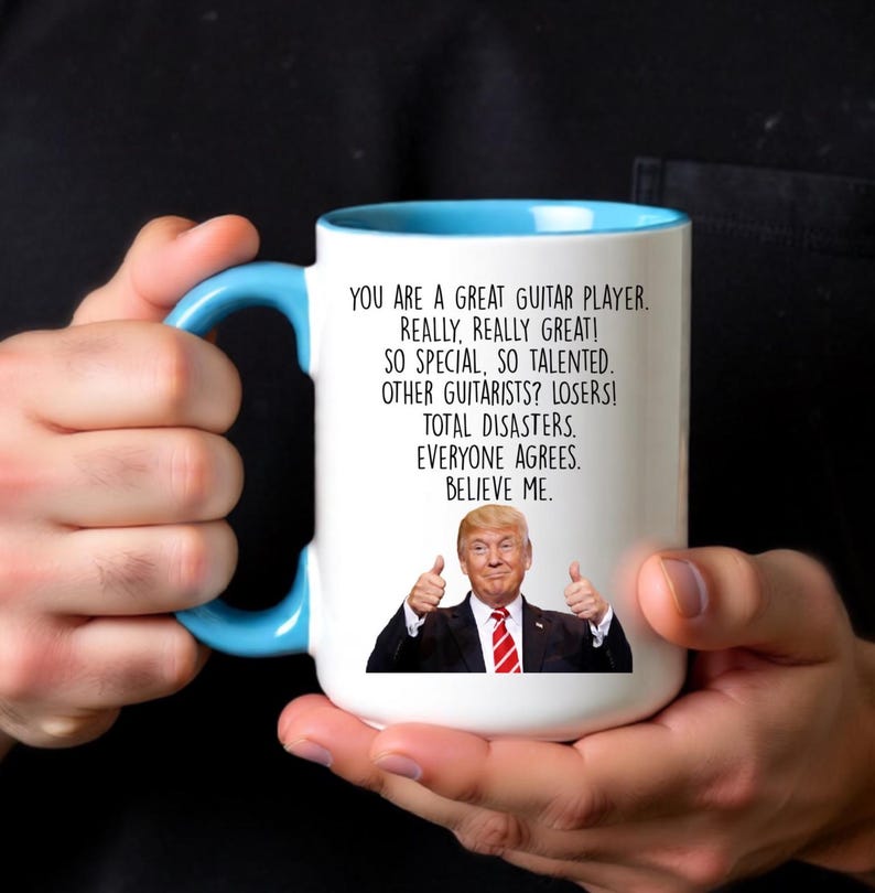 Puede incluir: Taza de cer&aacute;mica blanca con interior y asa azul claro. La taza presenta el texto "YOU ARE A GREAT GUITAR PLAYER. REALLY, REALLY GREAT!" y una imagen de un hombre haciendo una se&ntilde;al de pulgar.