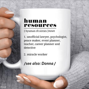 May include: White ceramic mug with black text that reads "human resources [hyumən r&egrave;-sorses] noun 1. unofficial lawyer, psychologist, peace maker, event planner, teacher, career planner and detective 2. miracle worker /see also: Donna/"