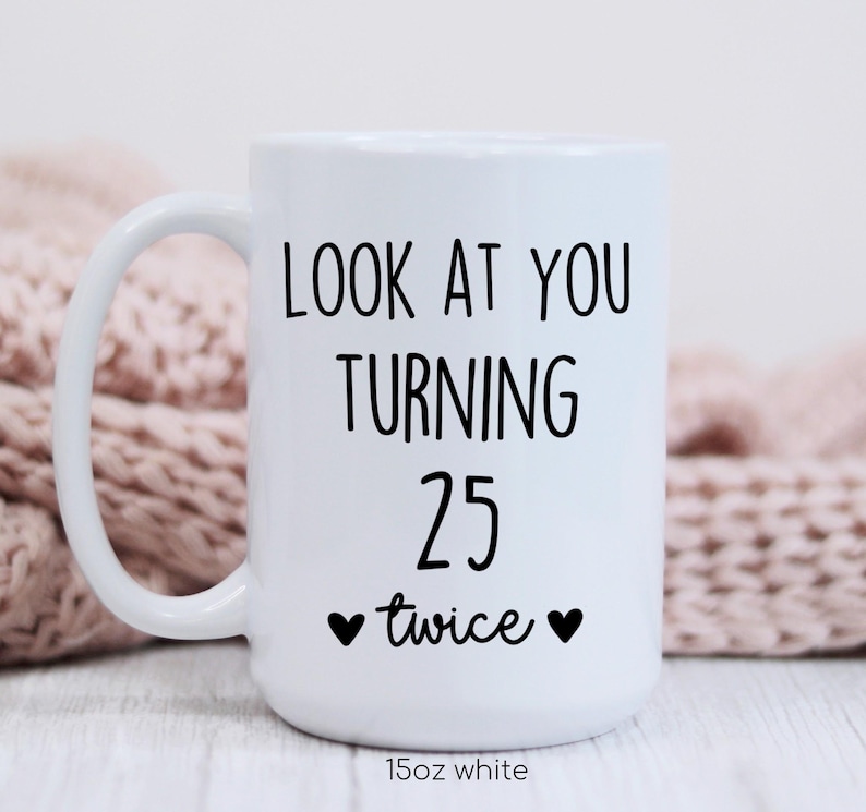 May include: White ceramic mug with a curved handle. The mug features black text that reads "LOOK AT YOU TURNING 25 twice" with two black hearts. The bottom of the mug reads "15oz white".