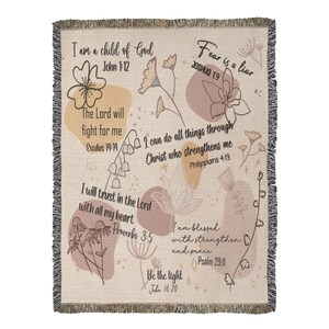 May include: Woven throw blanket with a cream background, featuring floral illustrations and inspirational quotes in black text. The design includes quotes like "Fear is a liar" and "I am a child of God". The blanket has a fringed edge.