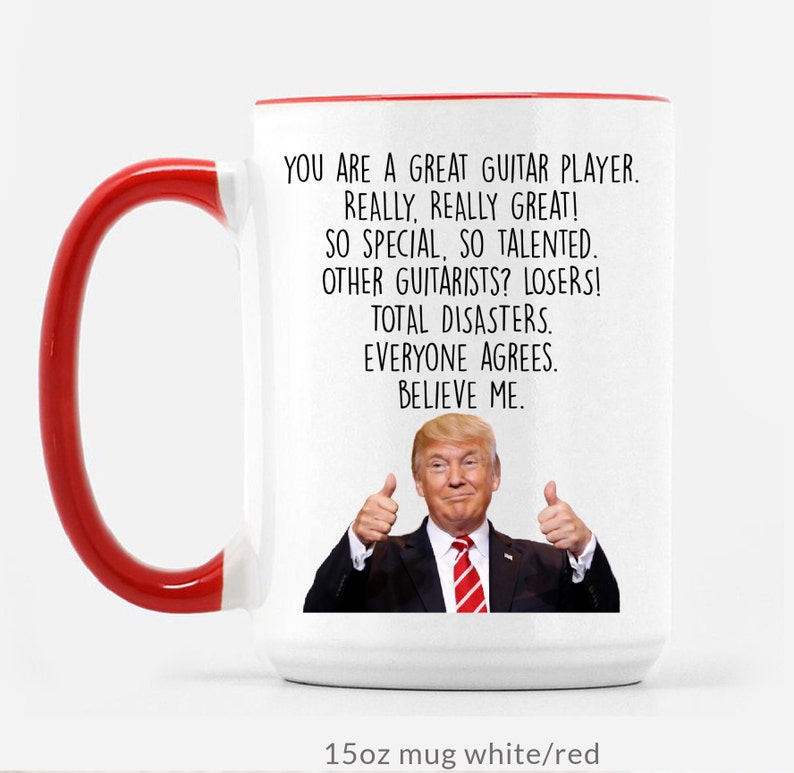 Puede incluir: Taza de cer&aacute;mica blanca con interior y asa rojos. La taza presenta el texto "YOU ARE A GREAT GUITAR PLAYER. REALLY, REALLY GREAT!" y una imagen de un hombre con el pulgar hacia arriba. La taza es de 425 ml.