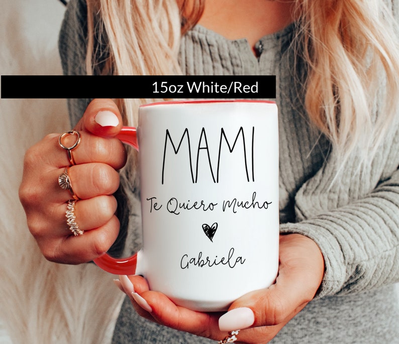 May include: White ceramic mug with a red rim. The mug has black text that reads "MAMI Te Quiero Mucho" with a small heart and the name "Gabriela" underneath.