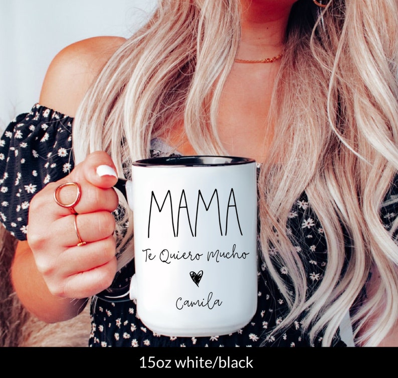 May include: White ceramic mug with a black rim and handle. The mug has black text that reads "MAMA Te Quiero Mucho" with a black heart and the name "Camila" underneath.