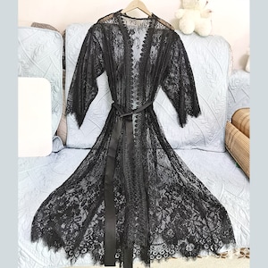 May include: A black lace robe with a satin sash. The robe has a long, flowing silhouette and delicate lace detailing.