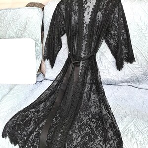 May include: A black lace robe with a satin tie belt. The robe has a delicate floral pattern and a scalloped hem.