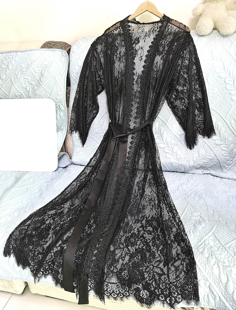 May include: A black lace robe with a satin tie belt. The robe has a delicate floral pattern and a scalloped hem.
