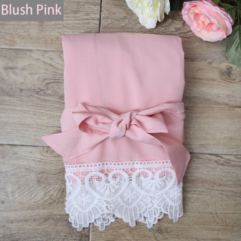 May include: A folded blush pink fabric garment featuring a matching fabric tie at the center and a wide band of intricate white lace trim along the bottom edge. The text Blush Pink is visible in the upper left corner of the image.