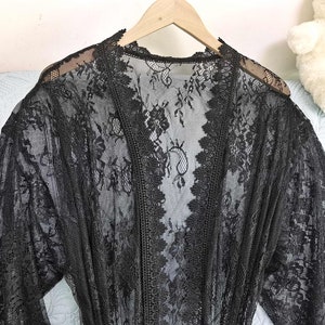 May include: Black lace robe with long sleeves and a V-neckline. The robe is made of delicate lace and has a sheer, flowing design.