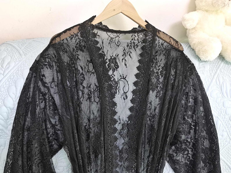 May include: Black lace robe with long sleeves and a V-neckline. The robe is made of delicate lace and has a sheer, flowing design.