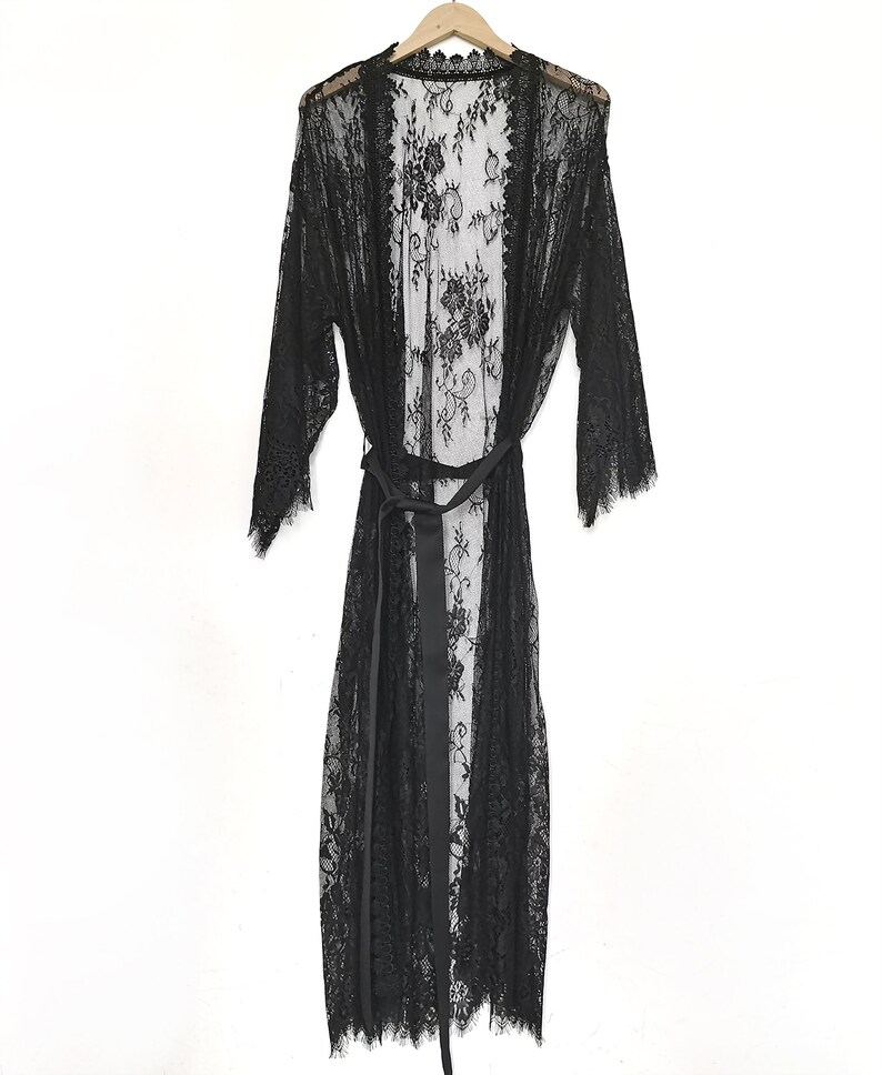 May include: A black lace robe with a satin tie belt. The robe has a long, flowing silhouette and a delicate floral pattern.